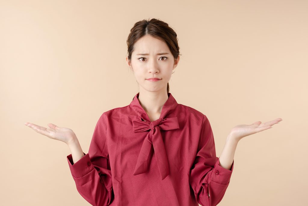 困った表情で両手を広げ、迷っている様子の女性